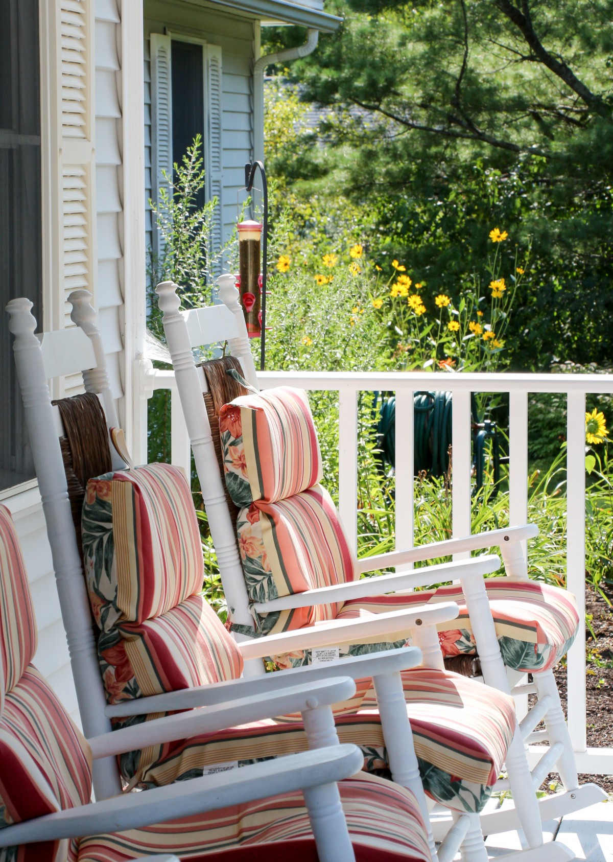 A cozy porch with striped cushioned rocking chairs overlooking a garden.