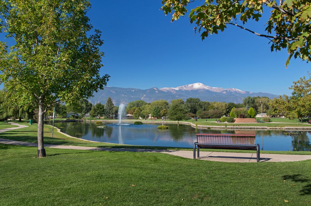 Scenic view of a park with a lake, fountain, and mountains in the background.