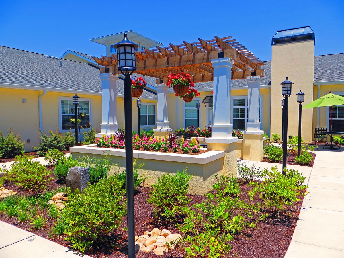 A beautifully landscaped garden featuring a pergola with hanging flowers and ornate lamp posts.