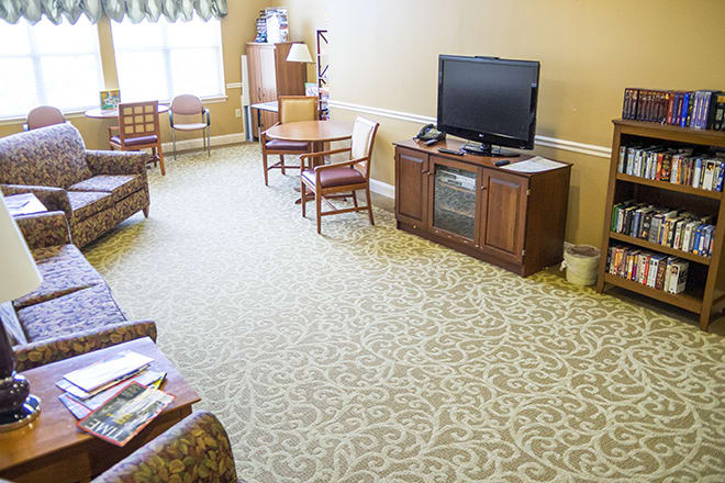 A well-lit living room with a television, chairs, and a table on a carpeted floor.