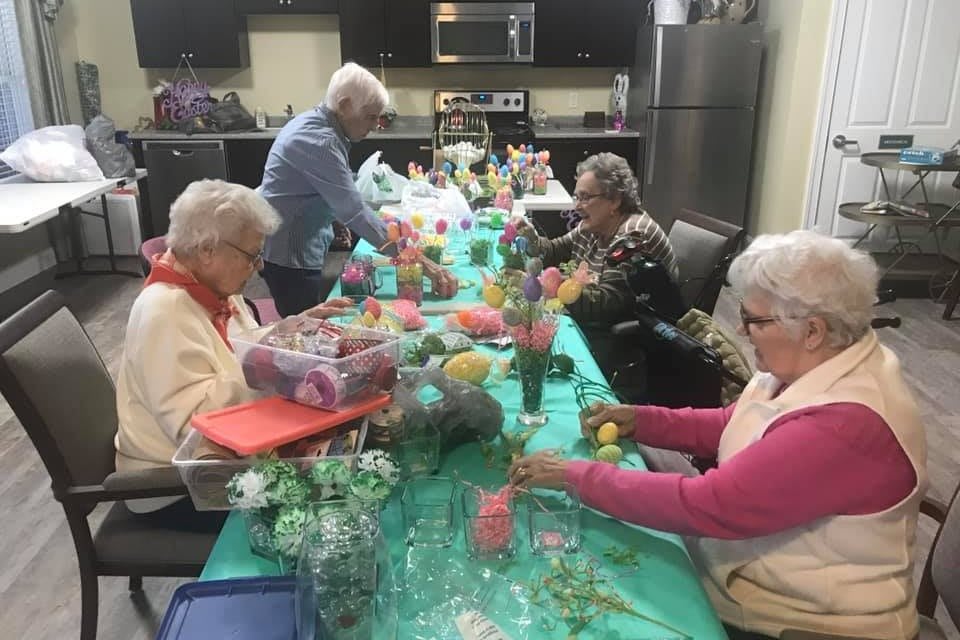 A group of seniors engaged in a crafting activity with flowers at a table.