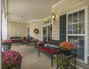 A cozy porch with benches, potted flowers, and large windows for a welcoming outdoor space.