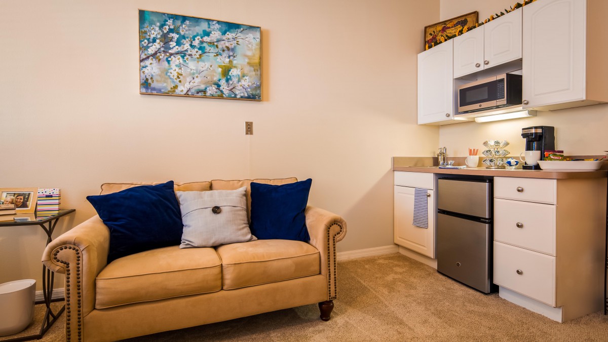 A cozy living area with a beige sofa and a compact kitchenette, adorned with modern artwork.