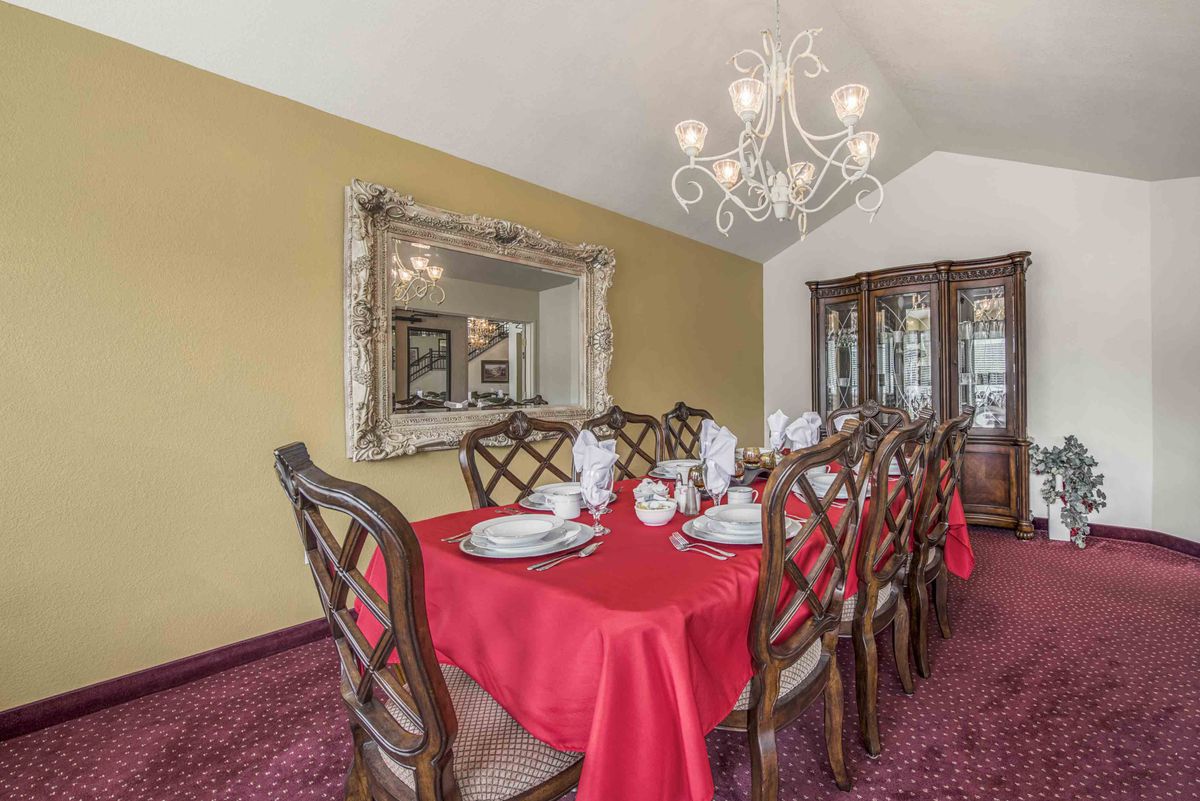 A beautifully set formal dining room with a red tablecloth and an elegant chandelier.