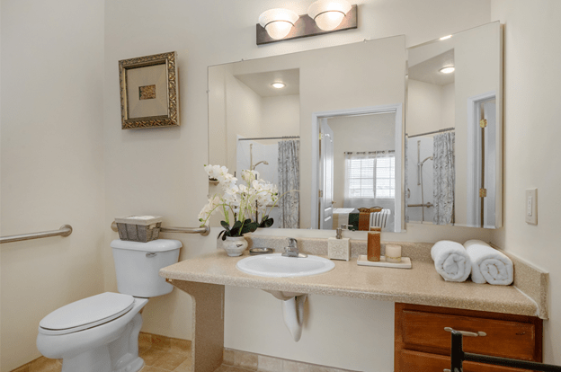A modern bathroom with a large mirror, sink, and decorative flowers on the countertop.