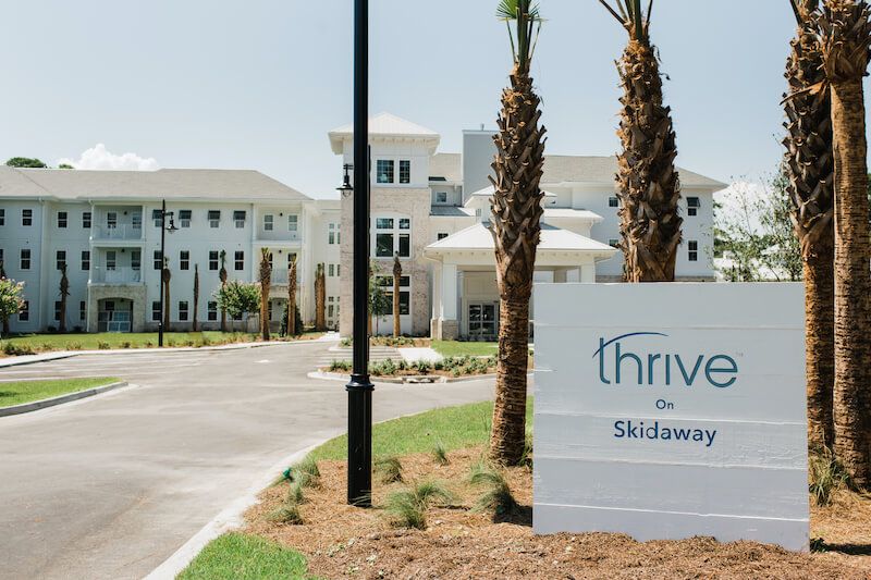 Entrance to a residential building with palm trees and a 'Thrive on Skidaway' sign.