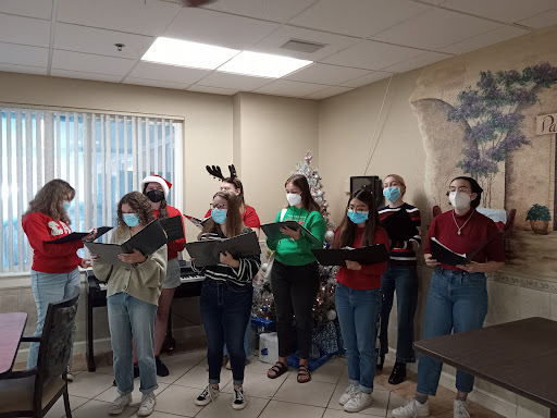 A choir dressed in festive attire performing Christmas songs while wearing masks.