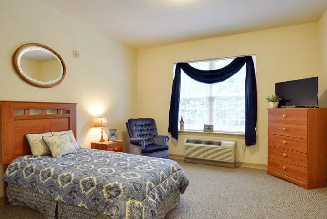 A cozy bedroom with a bed, chair, and window adorned with curtains.