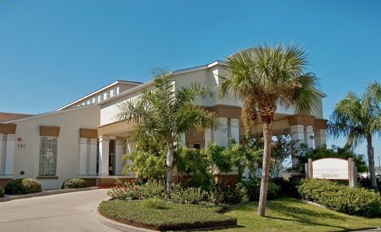 A modern residential house surrounded by palm trees and well-maintained landscaping under a clear blue sky.