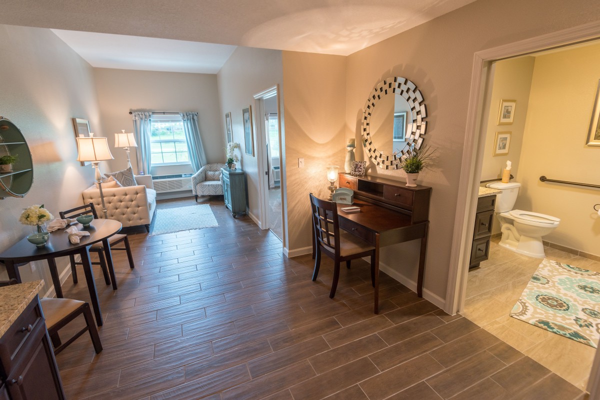 A cozy living space with a desk and mirror, featuring warm lighting and wooden flooring.