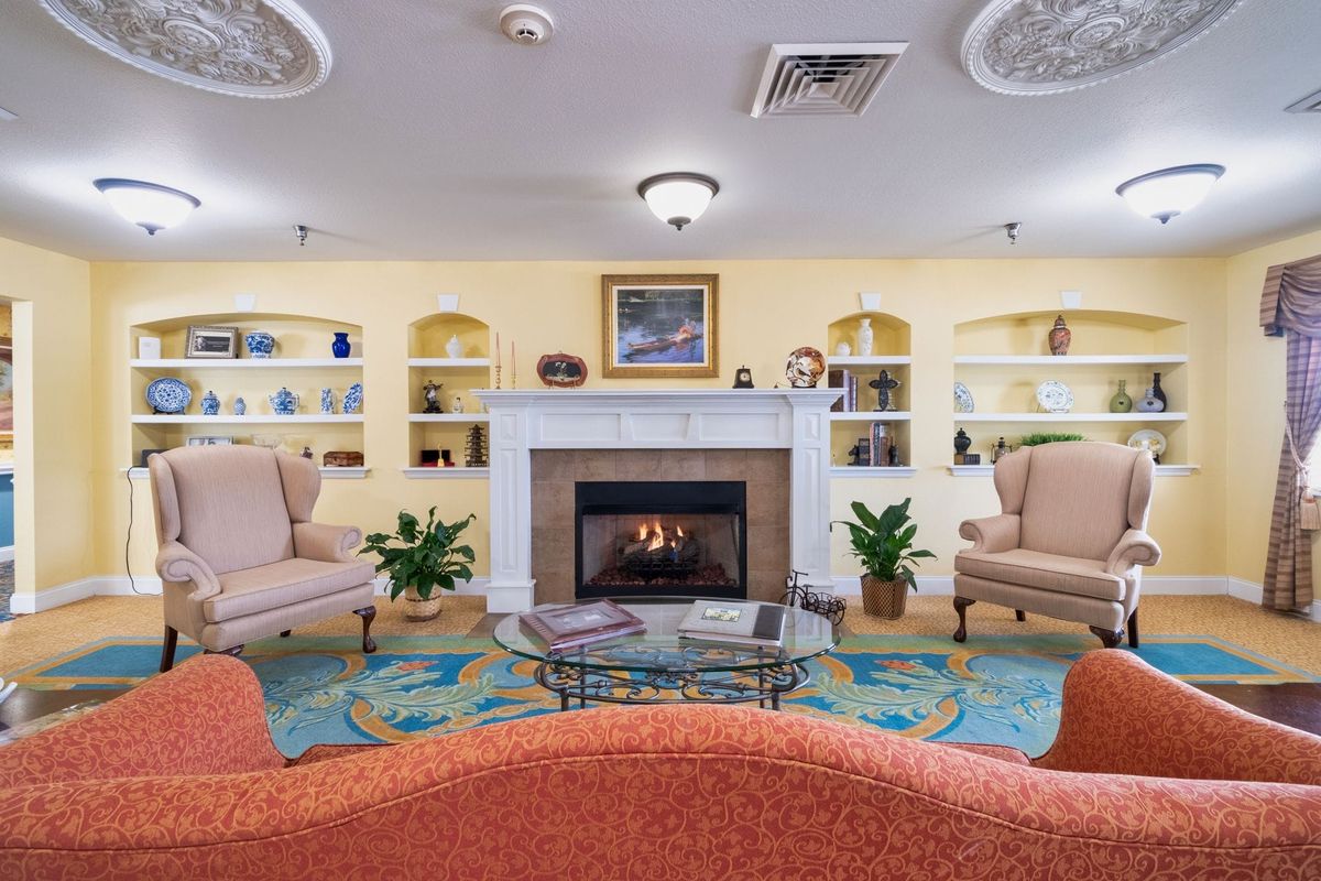 A cozy living room with a fireplace, surrounded by comfortable chairs and decorated shelves.