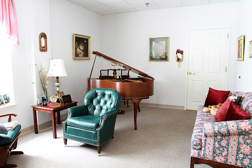 A cozy living room featuring a grand piano and a stylish green chair, adorned with artistic pieces on the walls.