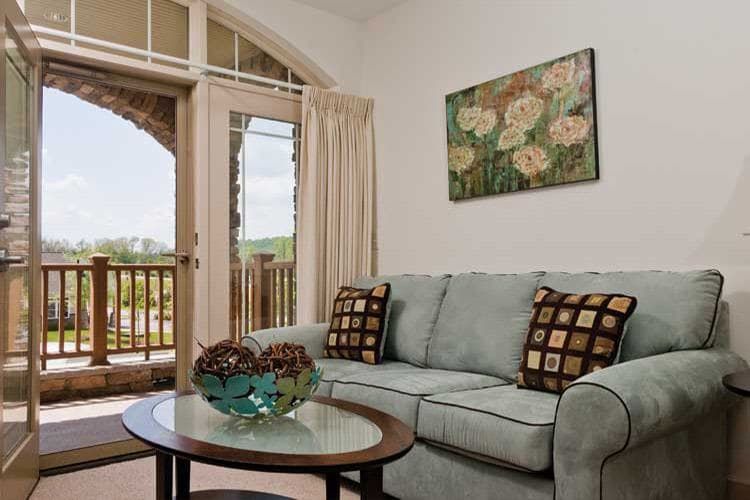 A cozy living room with a pastel sofa and floral artwork, featuring a coffee table and balcony access.