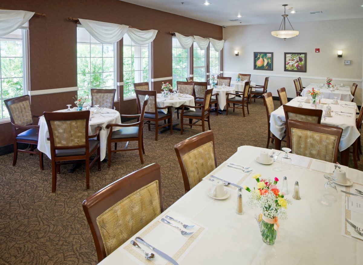 An elegantly set dining room with multiple tables and chairs, large windows, and tasteful decor.