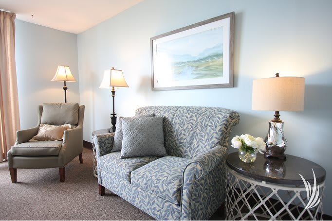 A cozy living room with patterned sofas, elegant lamps, and a landscape painting.