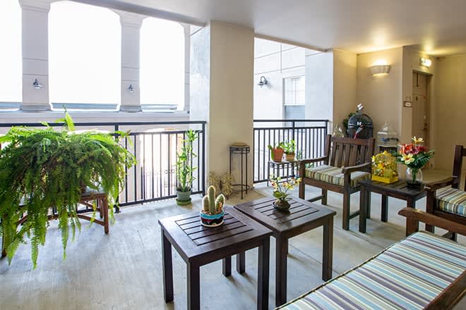 A well-decorated balcony featuring wooden furniture and green plants, creating a cozy outdoor seating area.