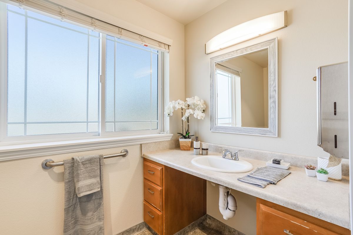 A bright bathroom with a large mirror, sink, and window allowing natural light.