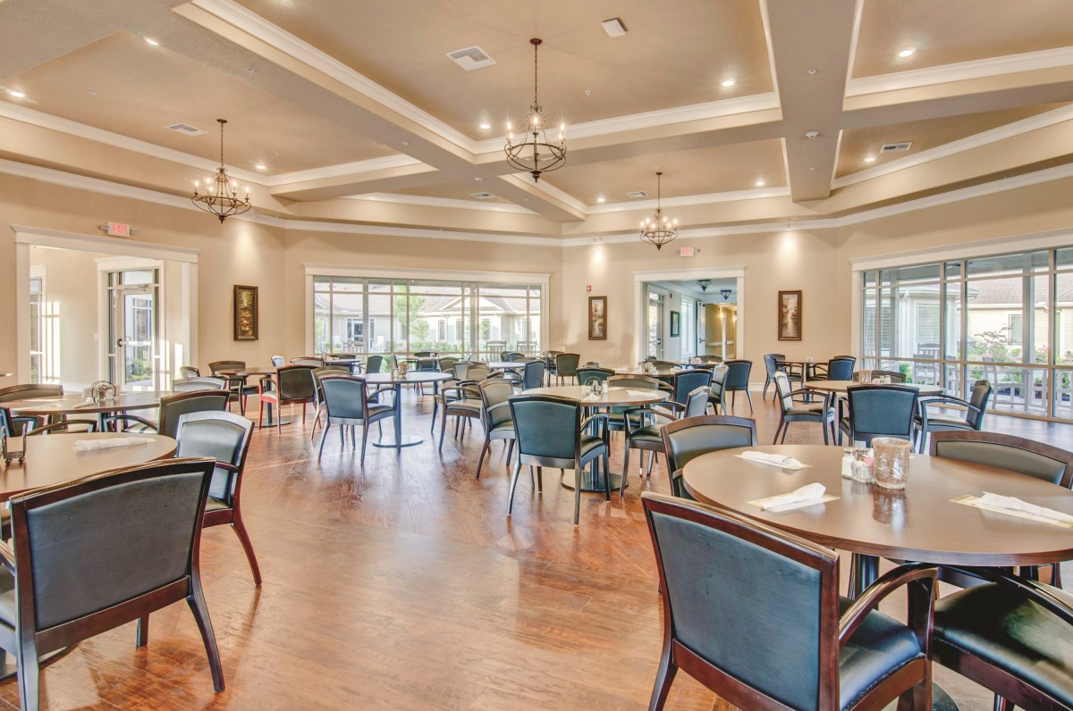 A spacious and elegantly designed restaurant dining area with well-arranged tables and chairs under bright chandeliers.