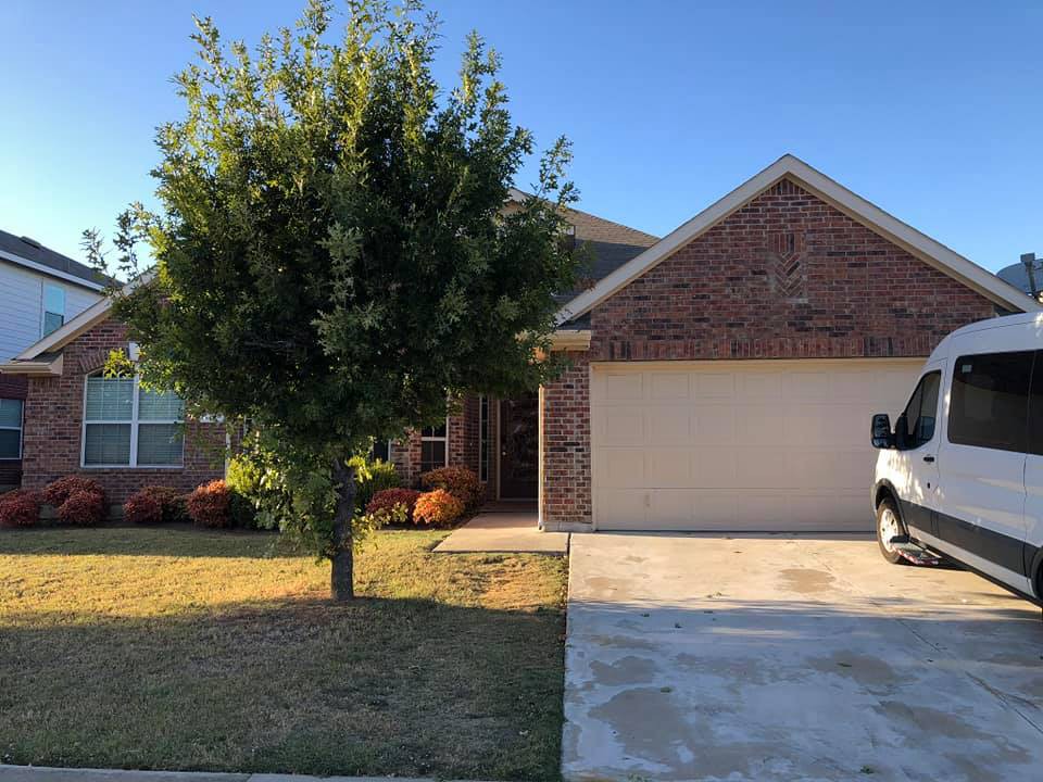 A suburban brick house with a driveway and a tree in the front yard.