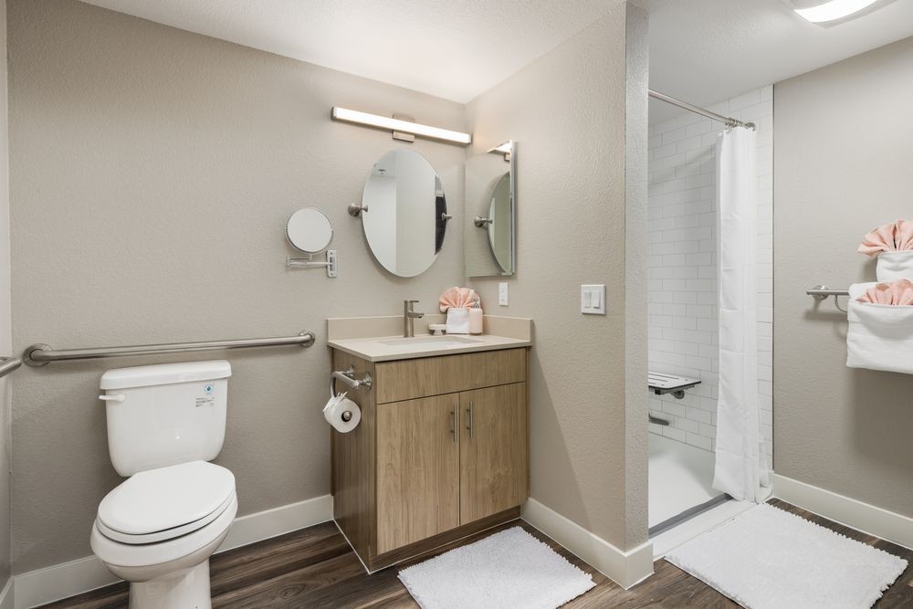 A modern bathroom with a wooden vanity, mirror, and walk-in shower.