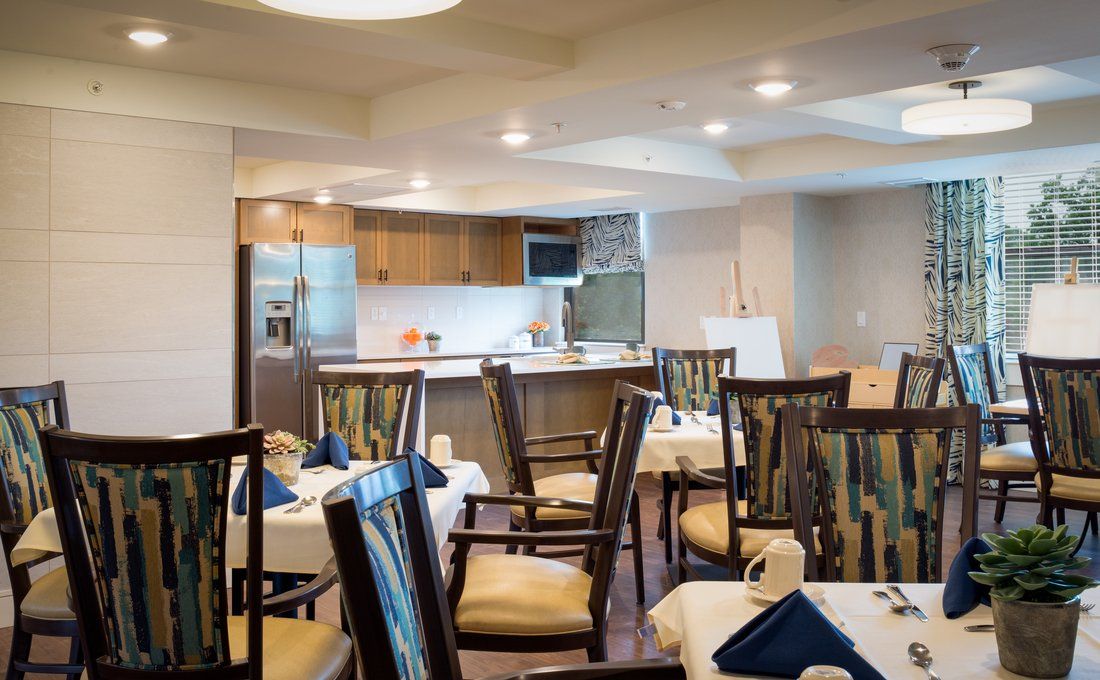A well-lit dining area with tables and chairs arranged near an open kitchen.