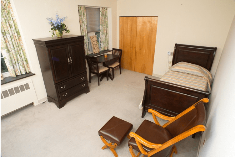 A cozy bedroom with wooden furniture including a bed, chairs, a table, and a dresser.