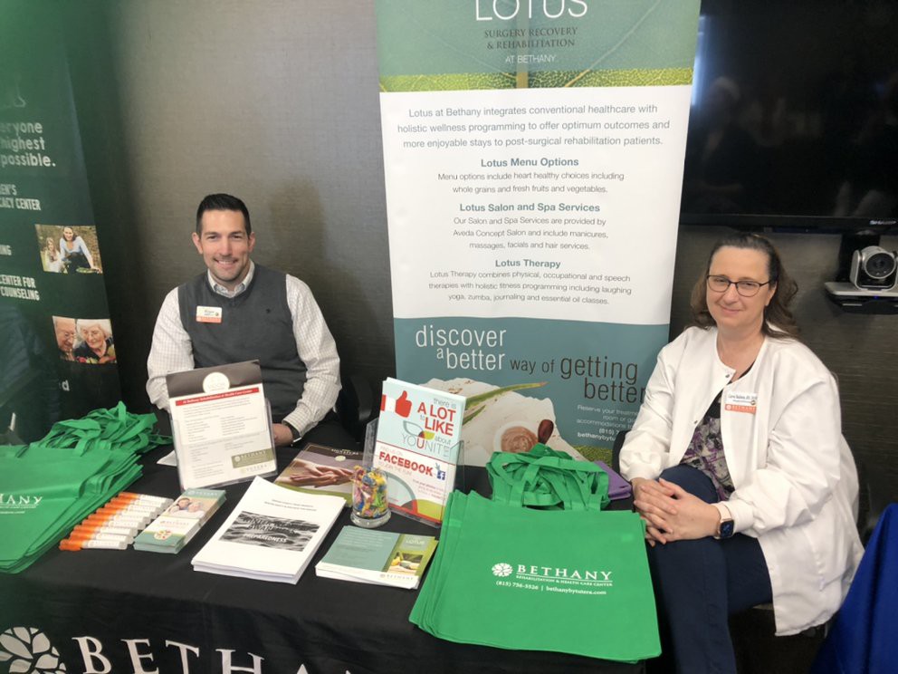 Two individuals sitting at an informational booth with promotional materials and bags on display.