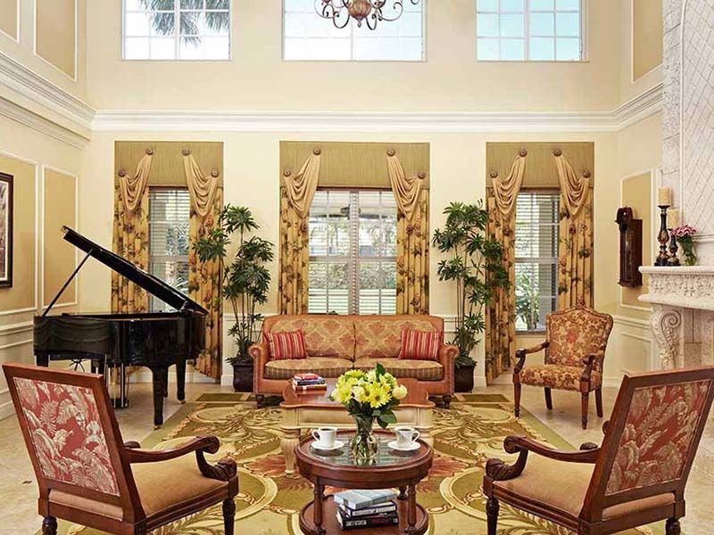 A spacious living room with elegant traditional decor, featuring a grand piano and ample natural light.