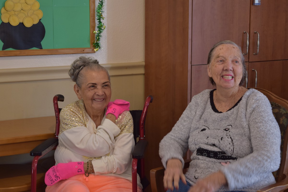 Two elderly women smiling and enjoying each other's company indoors.