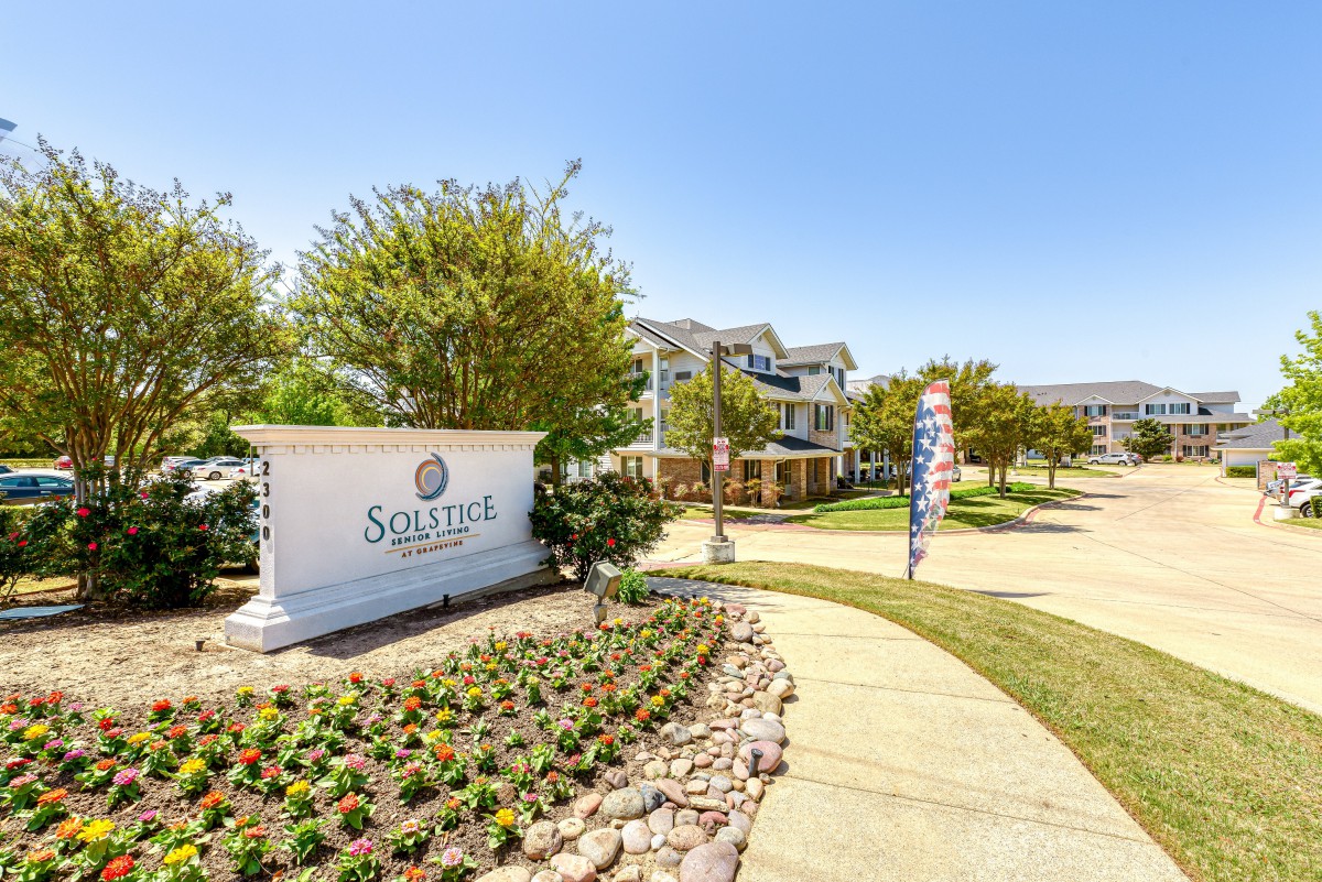 A well-landscaped entrance to an apartment complex with a prominent sign and manicured gardens.