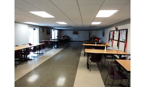 An empty cafeteria with tables and chairs arranged neatly under bright overhead lighting.