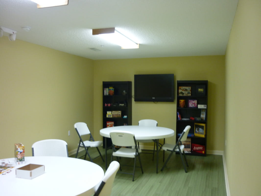 A small meeting room with tables, chairs, a TV, and bookshelves filled with games.