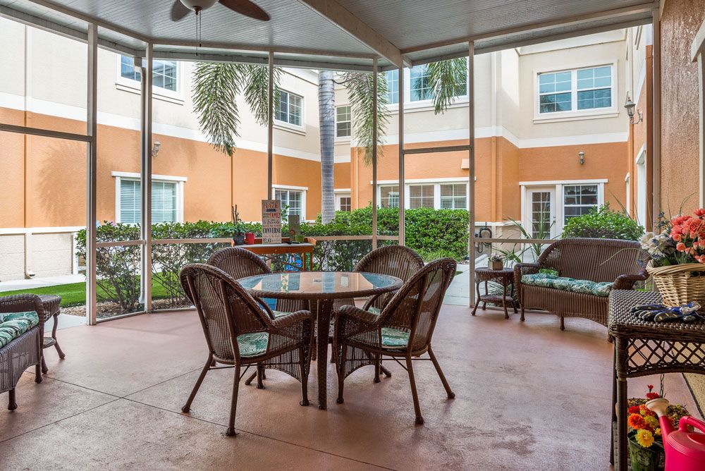 A cozy patio with outdoor seating in a screened area, surrounded by greenery and the exterior of a building.