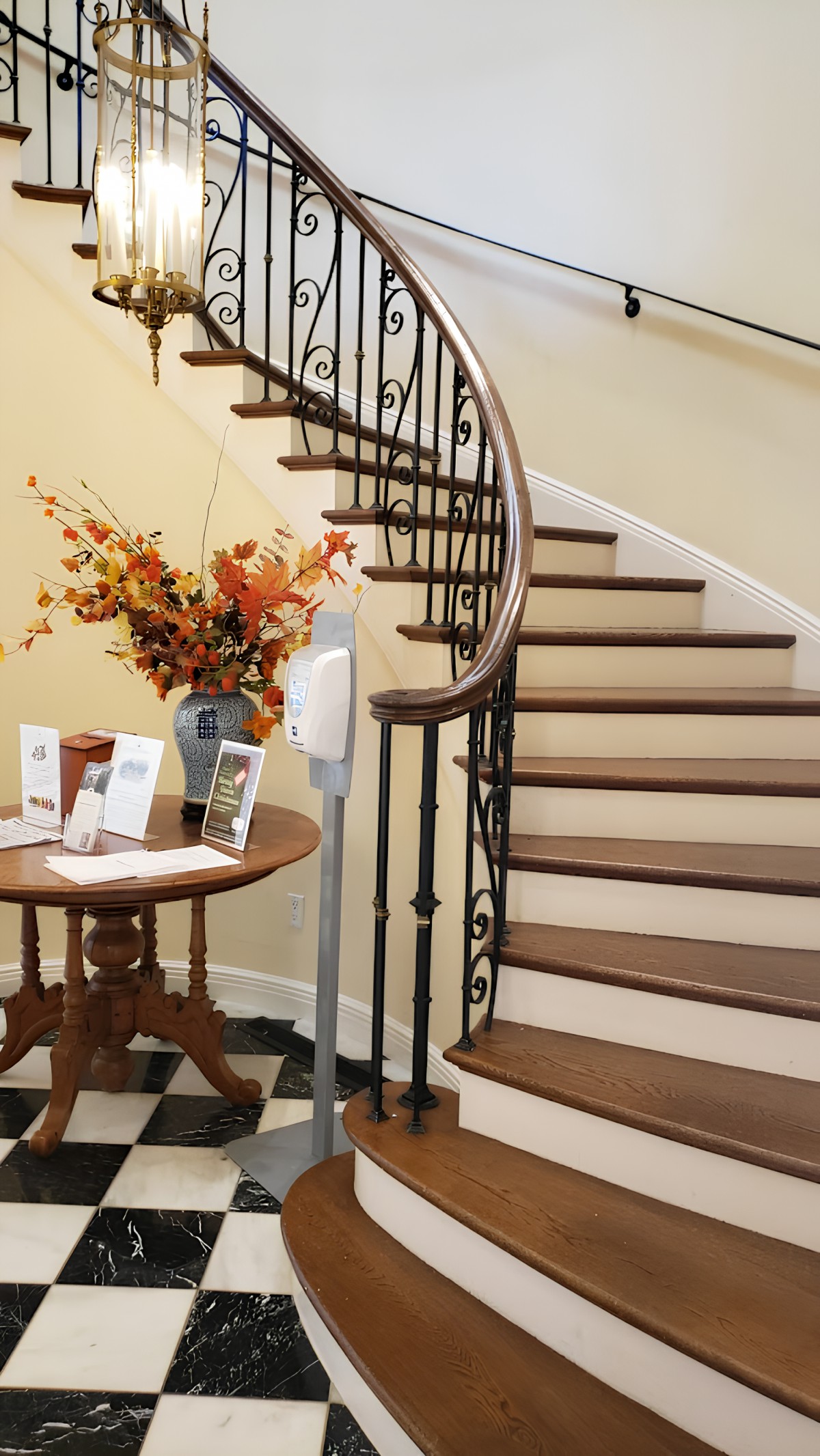 A cozy entrance hall with a spiral staircase and a table displaying brochures next to a hand sanitizer dispenser.