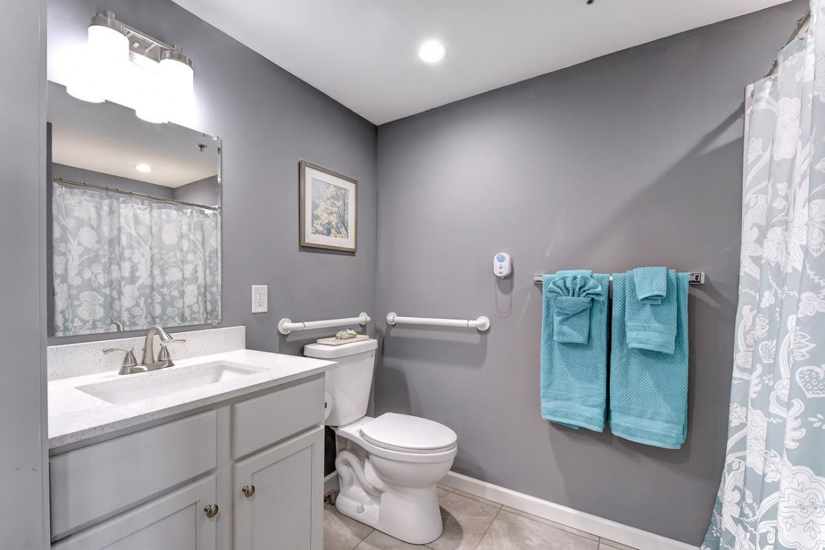 A modern bathroom with gray walls, featuring a toilet, sink, mirror, and turquoise towels.