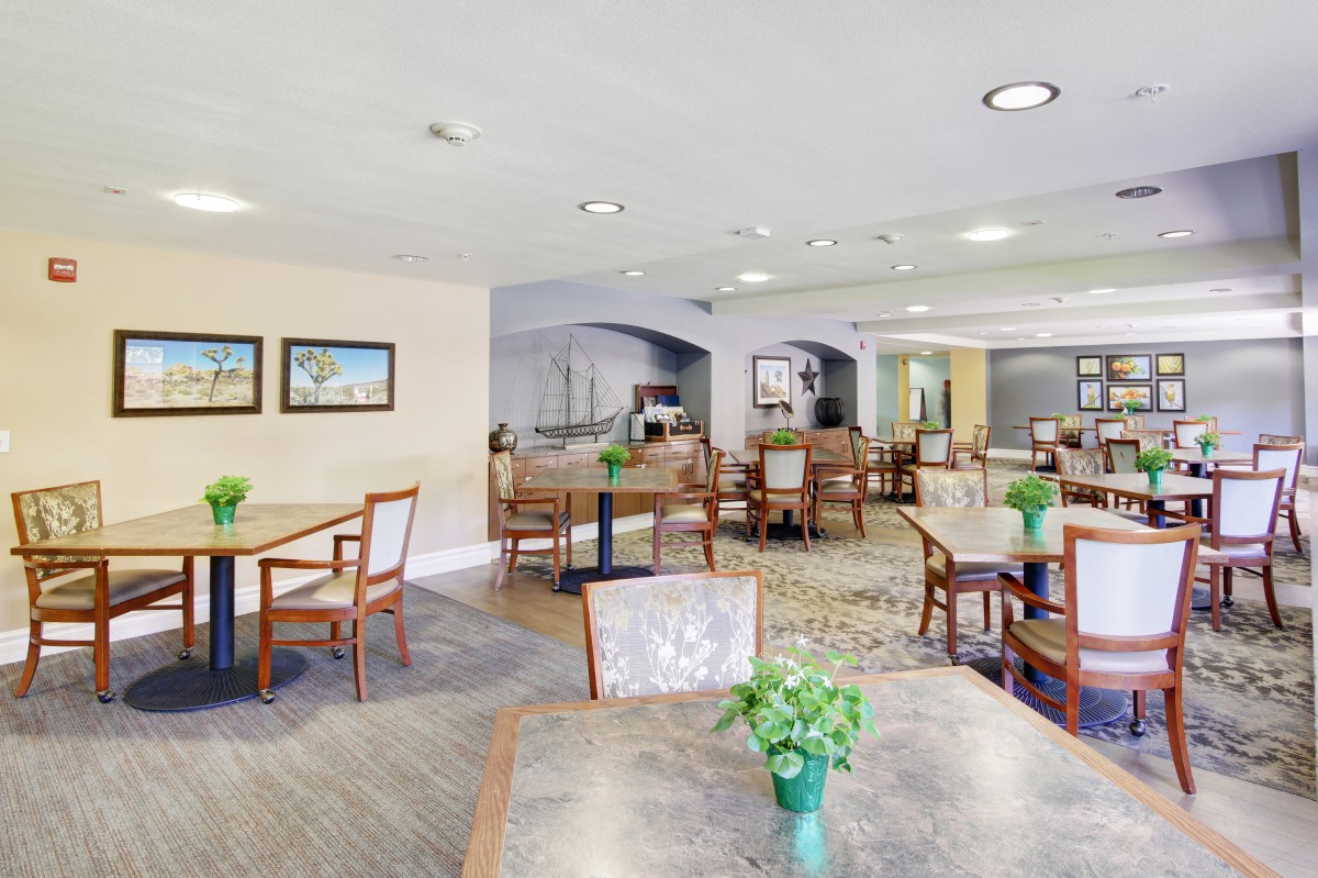 A well-lit dining area with wooden tables and chairs, decorated with indoor plants.