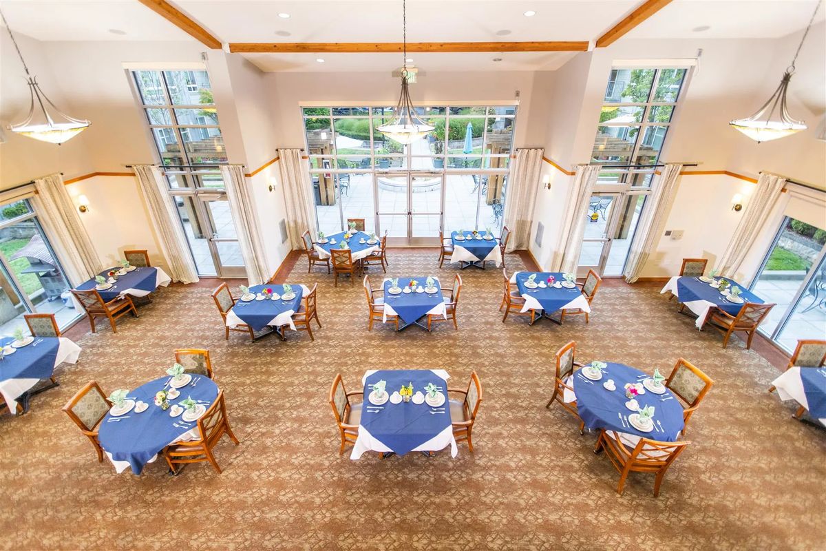 A bright event space with tables set for dining, featuring blue tablecloths and natural lighting.