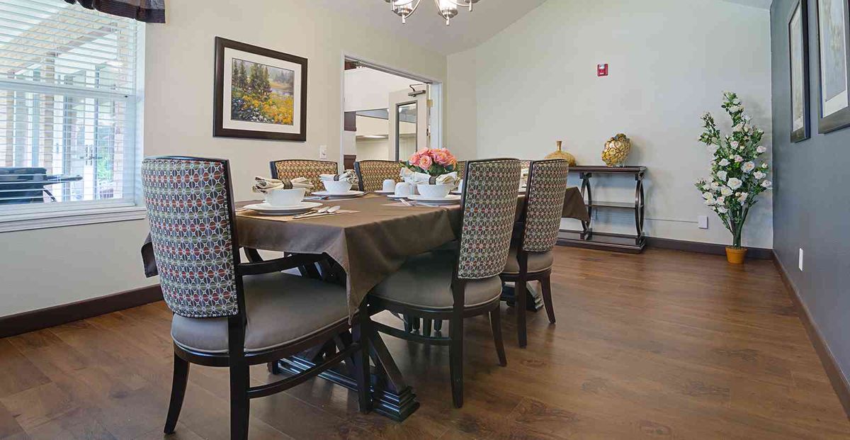 A cozy dining area set with a table and chairs, featuring a wall painting and kitchen access.