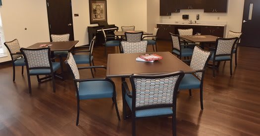 A cozy communal dining area with several tables and chairs, featuring a kitchenette in the background.