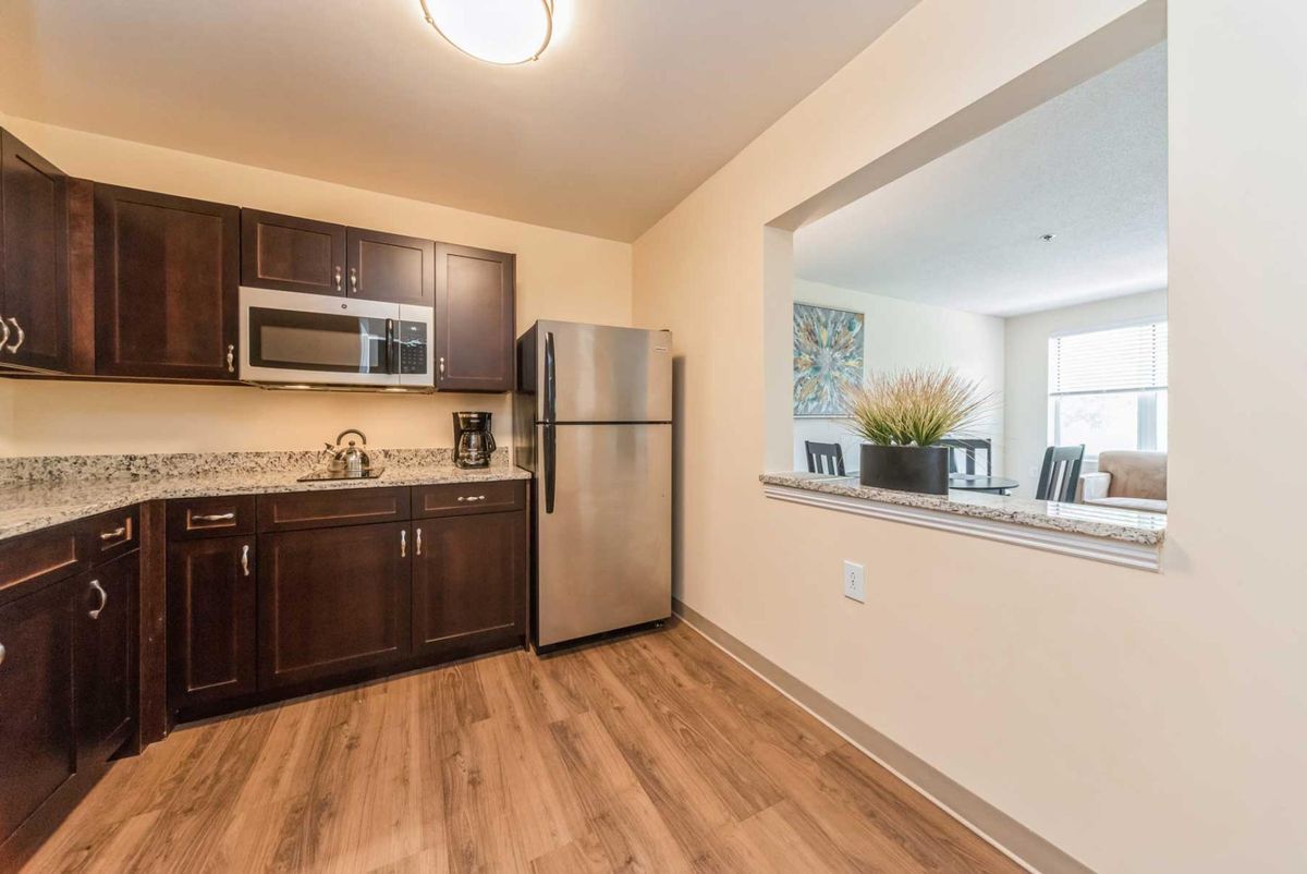 A modern kitchen with a stainless steel refrigerator, microwave, and wooden flooring.