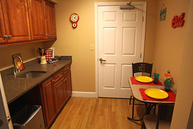 A cozy kitchen with wooden cabinets, a small dining table set for two, and a wall clock.