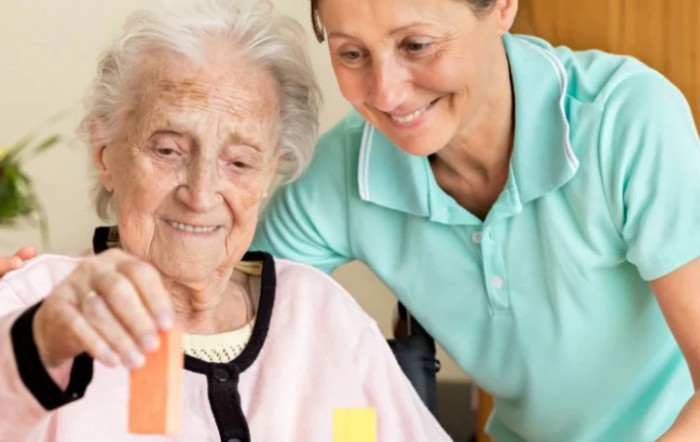 A caregiver assisting an elderly woman with a playful activity.