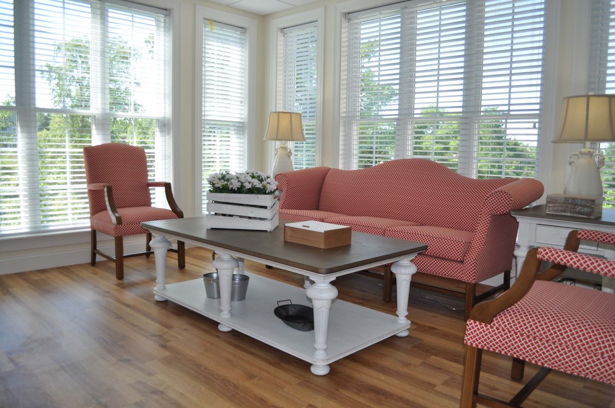 A cozy living room with pink sofas and armchairs, a white coffee table, and large windows letting in natural light.