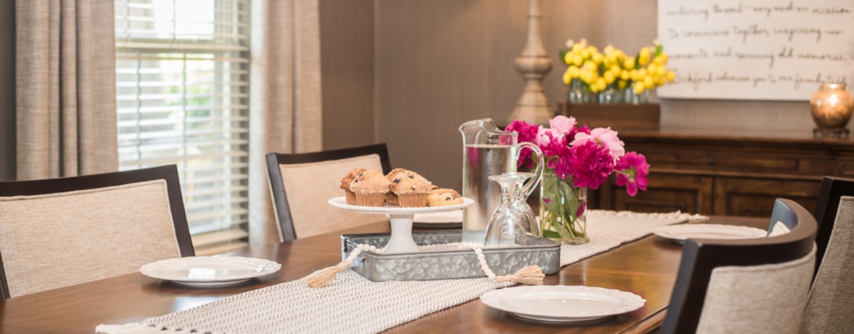 A cozy dining table setup with muffins, a water pitcher, and vibrant flowers.