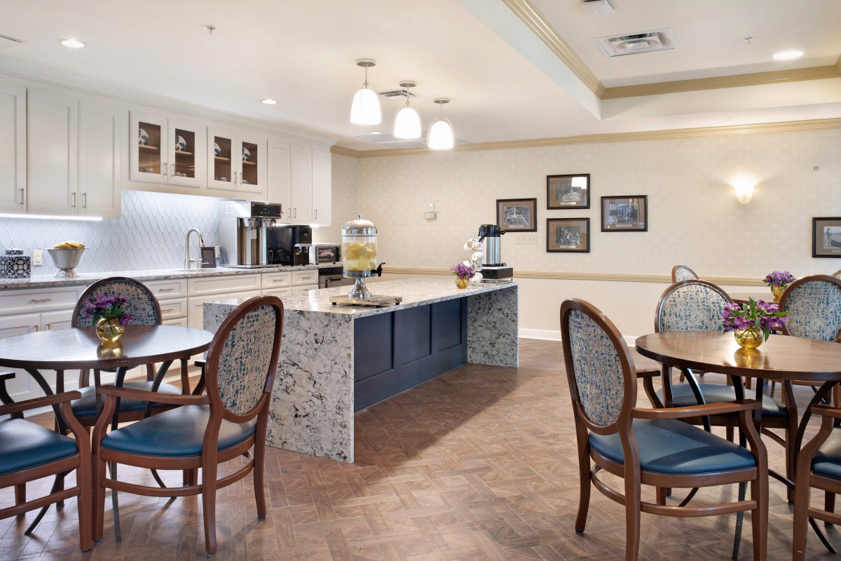 A cozy dining area with a modern kitchen setup, featuring round tables and elegant chairs.