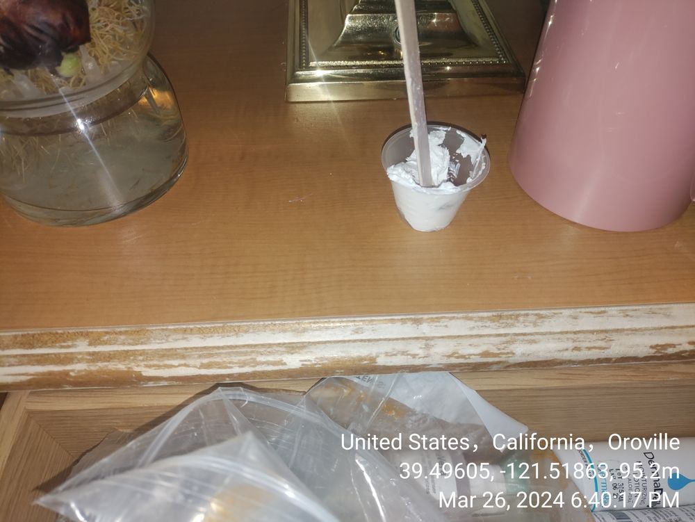 A small cup with a stirrer sits on a table next to a lamp.