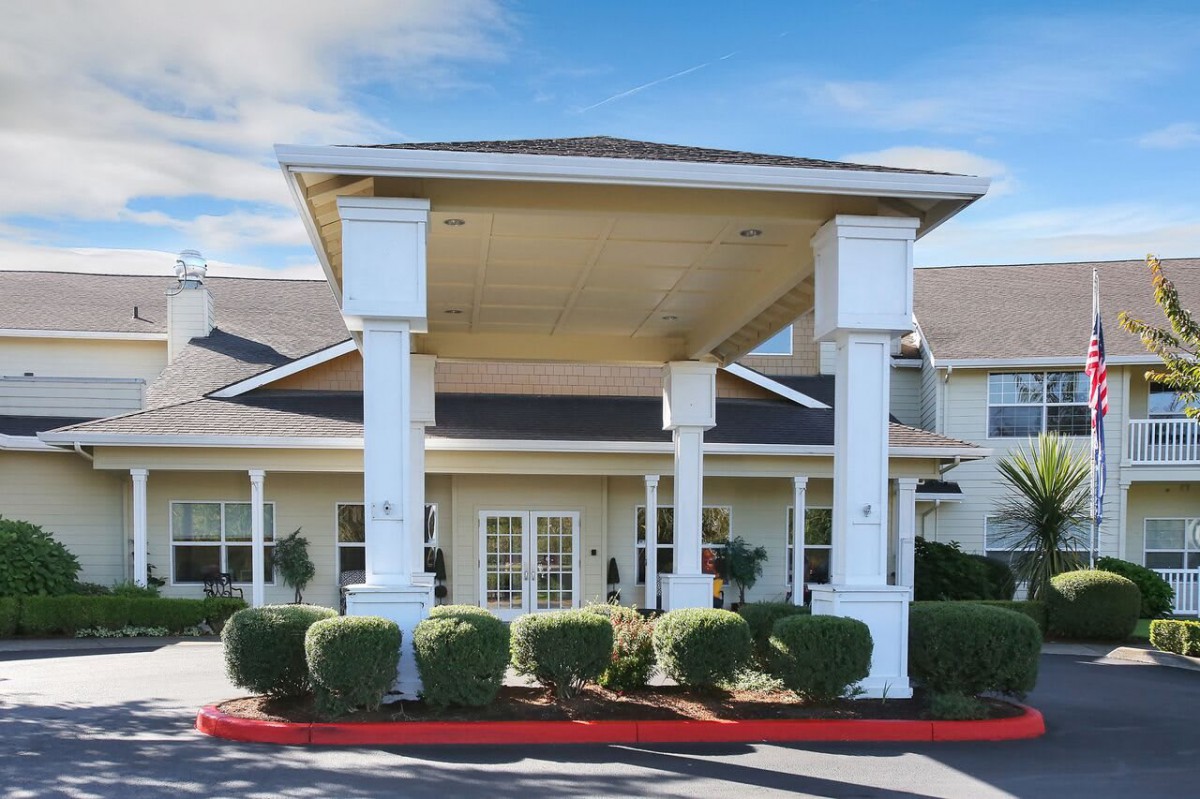 A residential building with a covered entrance featuring large white columns and landscaped shrubs.