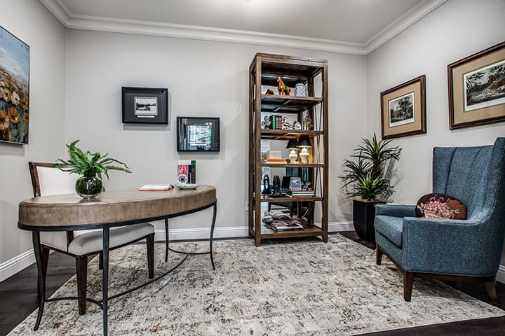 A cozy office space featuring a desk, bookshelf, armchair, and decorative plants.