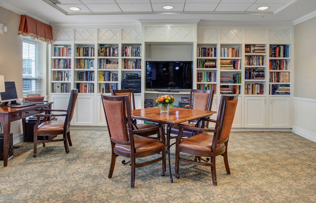 A cozy library room with a wooden table and chairs surrounded by bookshelves.