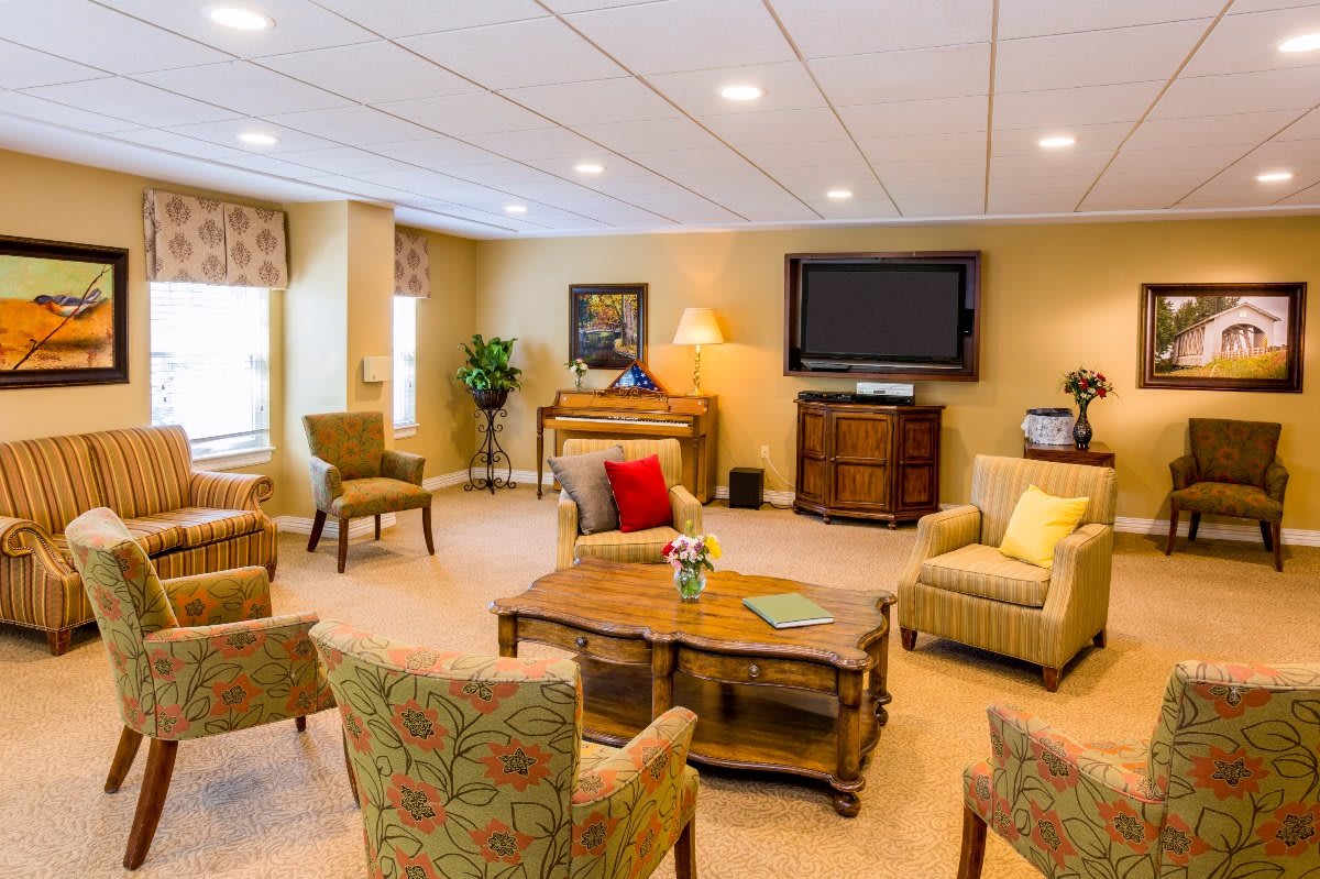 A cozy living room with various seating options and a large TV on the wall.